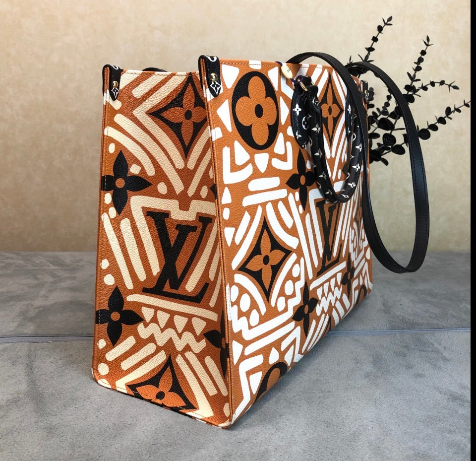 A Louis Vuitton tote bag featuring a bold geometric pattern in terracotta orange, white, and black. The bag has black leather handles and is displayed on a gray surface against a beige background.