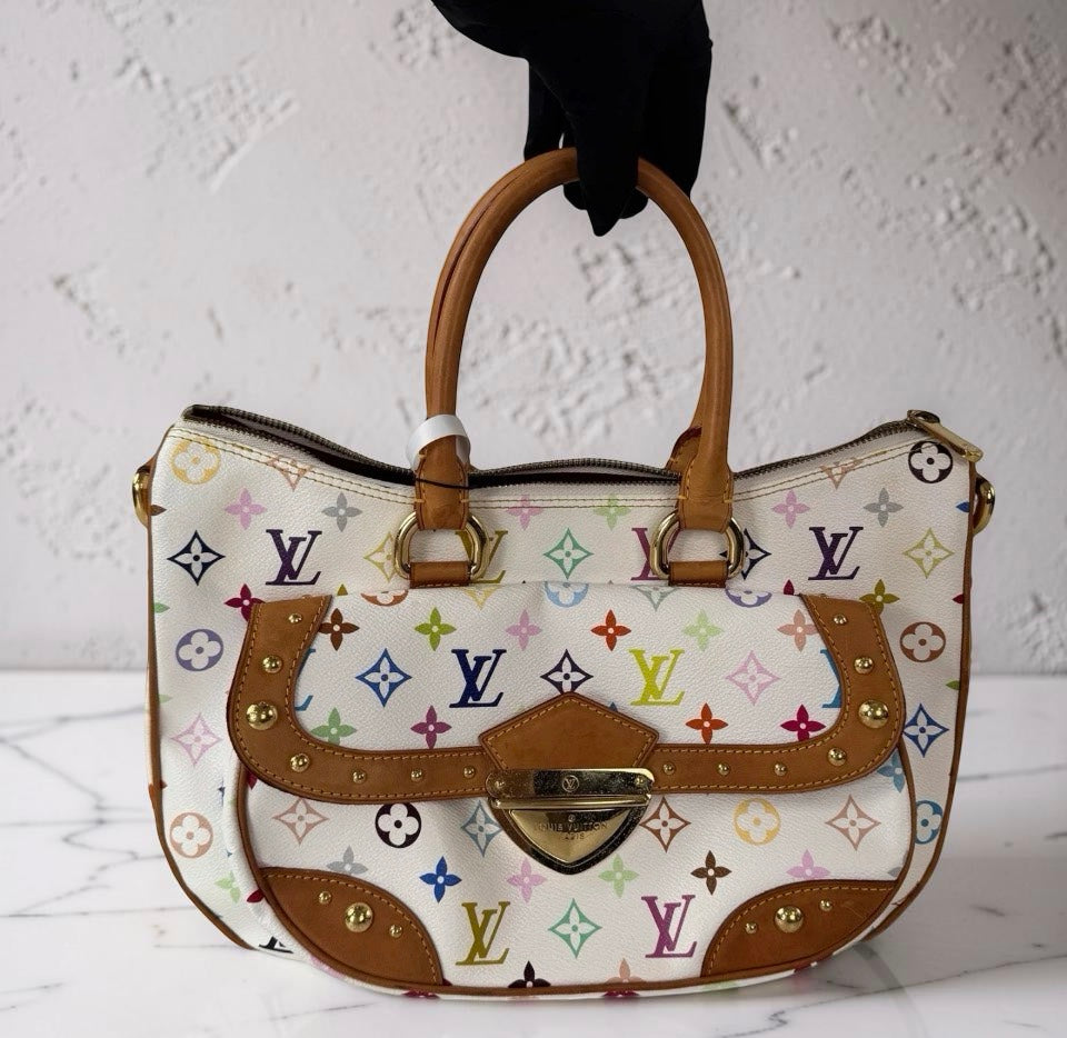 A Louis Vuitton monogram handbag with tan leather trim and double top handles, held by a black-gloved hand against a white textured wall and marble surface.